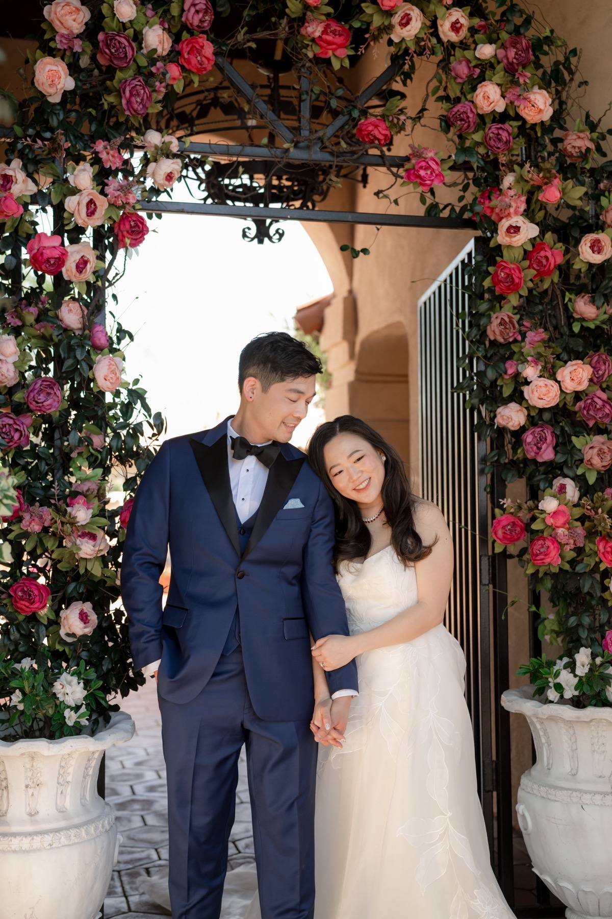 Michael Tran and Alice Chi under a floral arch, with his custom blue wedding tuxedo complementing her dress